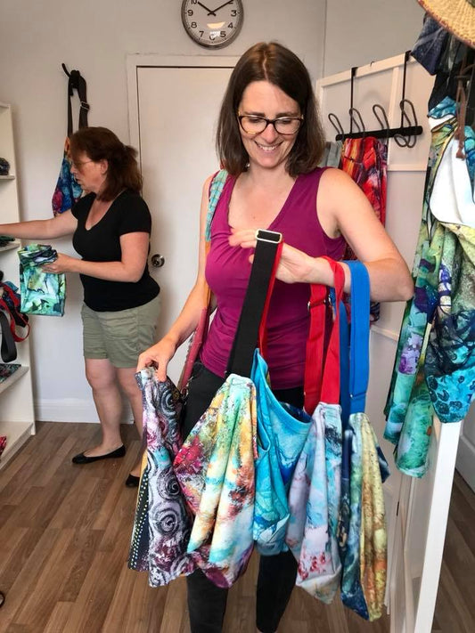 An Artist Generations customer holds up several tote bags trying to decide which one she would like to buy.